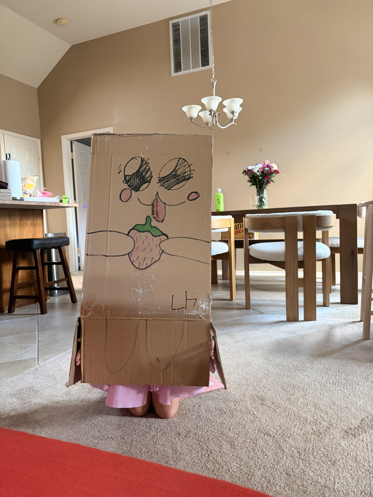 A child kneeling inside a tall cardboard box decorated with a face and a strawberry